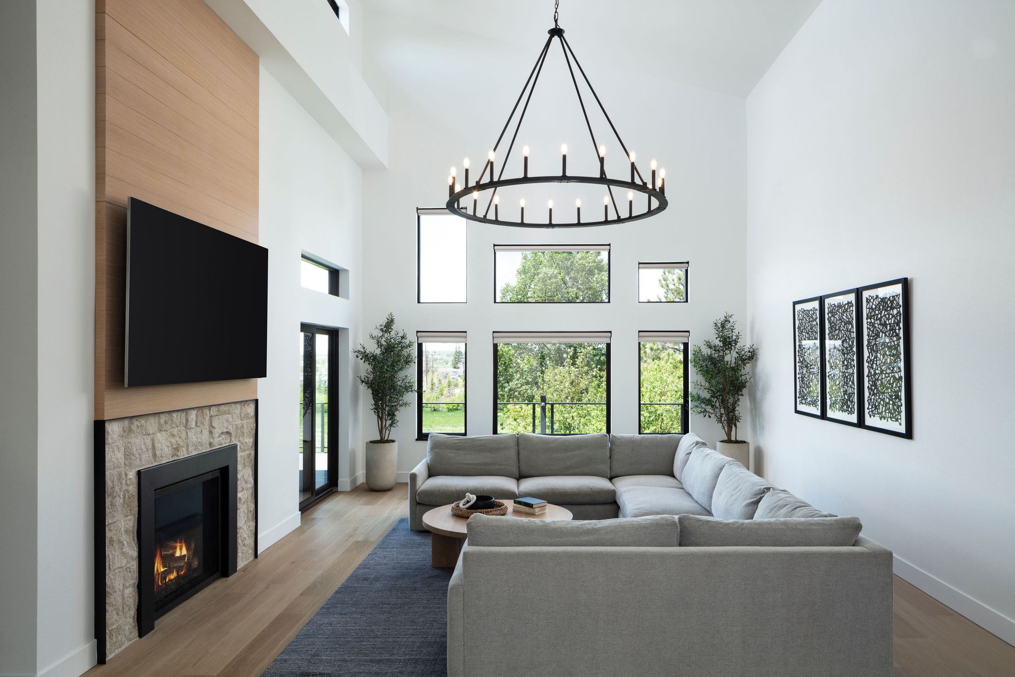Wildflower custom home - family room with minimalist gas fireplace with natural stone surround, wall-mounted TV, sliding glass doors to the deck outside.